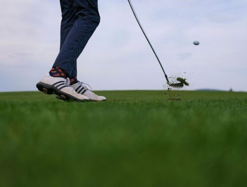 Golfschläger trifft den Ball knapp über dem Rasen im starken Wind