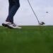 Golfschläger trifft den Ball knapp über dem Rasen im starken Wind